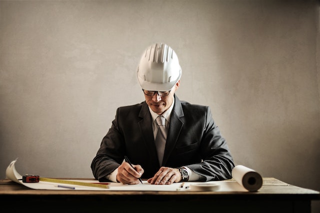 contractor in a suit and white hardhat looking at buildings floor plans